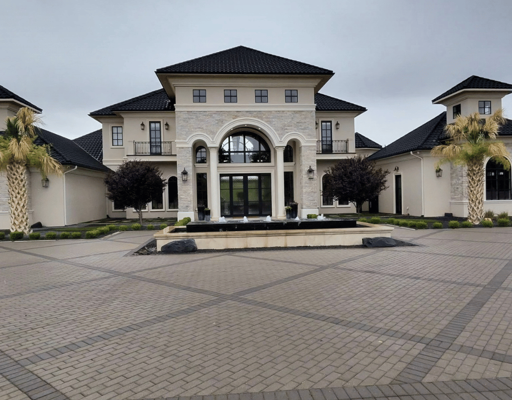 Large stone mansion with a paver courtyard, fountain, and palm trees