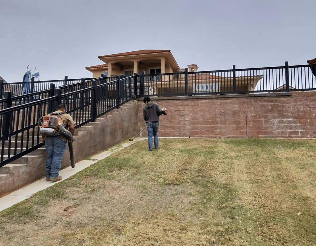 Two landscapers clearing debris and blowing grass clippings on a terraced hillside backyard