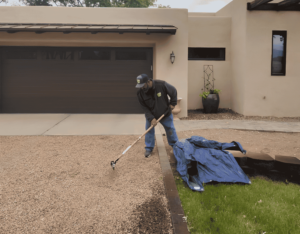 Landscaper spreading and raking gravel along a driveway edge in front of a modern home