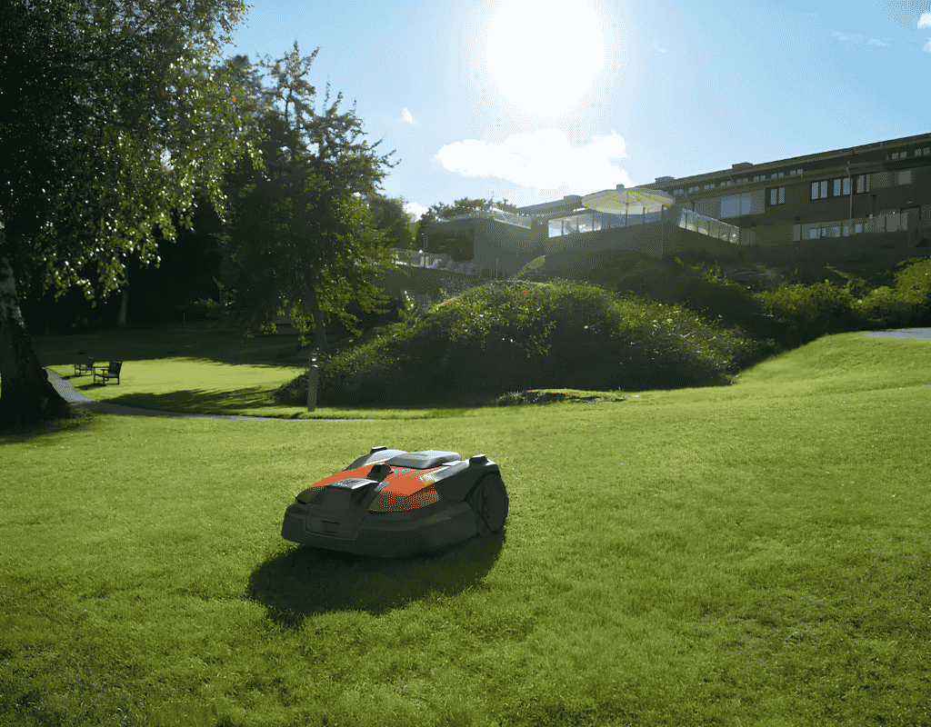 Robotic lawn mower parked on a grassy hillside with a building visible in the background